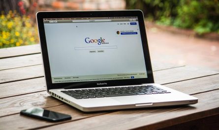 Laptop ouvert sur Google, smartphone à gauche, table en bois, jardin flou