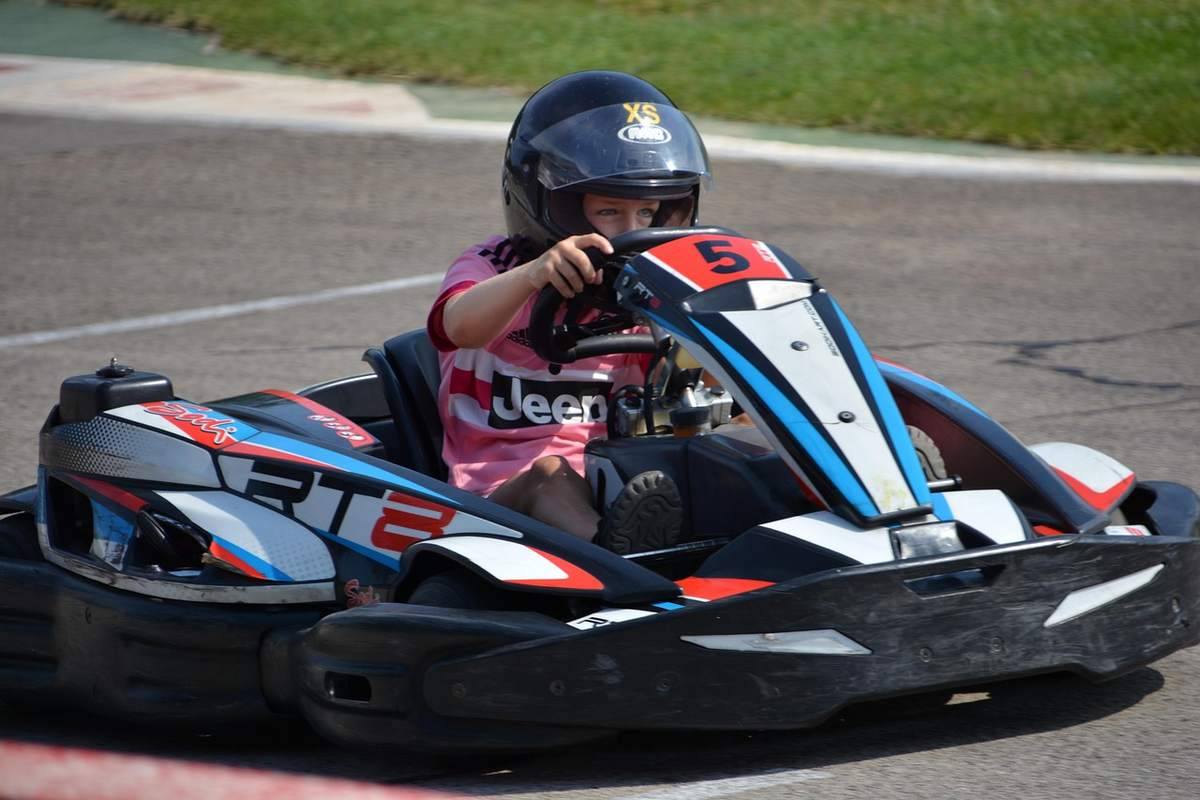 Un enfant pilote un kart de course sur piste, casque noir