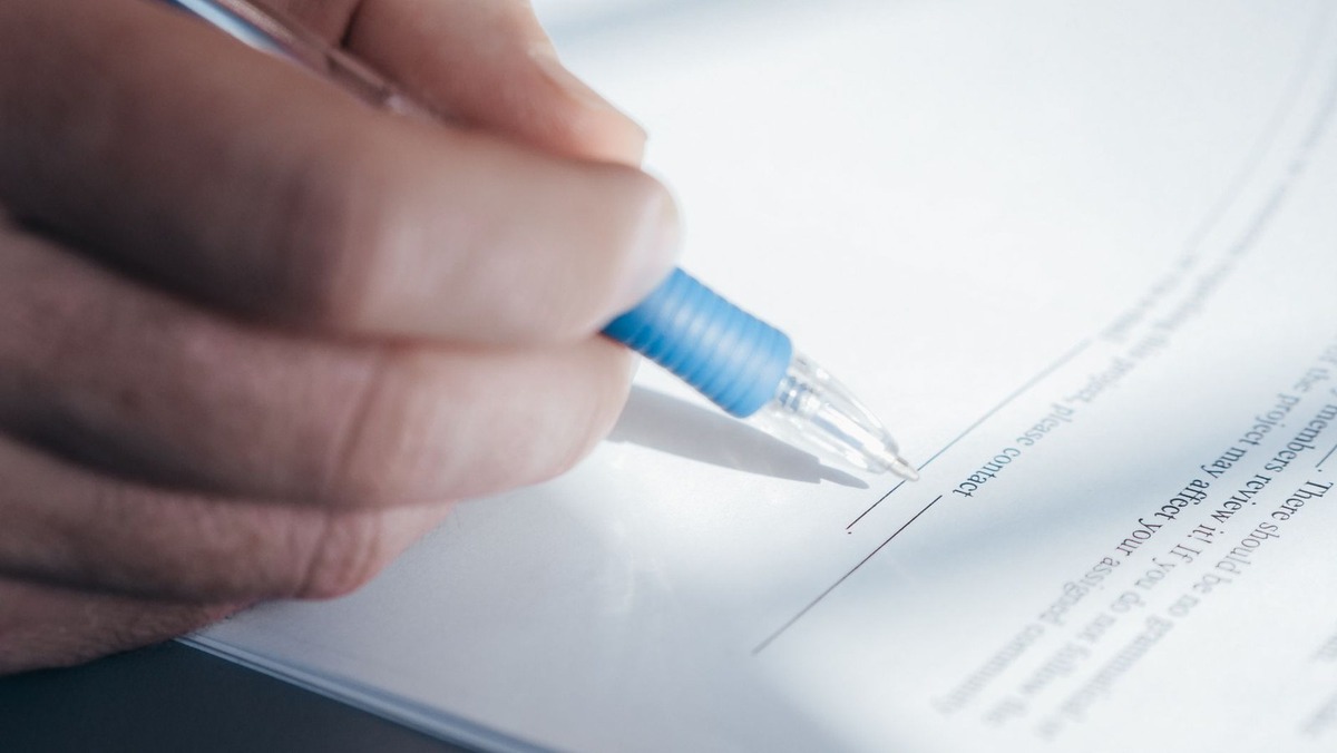 Main tenant un stylo bleu, en train de signer un document Main tenant un stylo bleu, en train de signer un document
