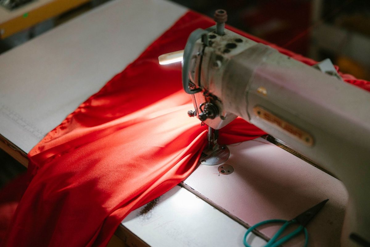 Machine à coudre blanche cousant un tissu rouge avec des ciseaux bleus à côté