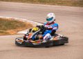 Un pilote en kart de course sur piste, vêtu d'une combinaison et casque