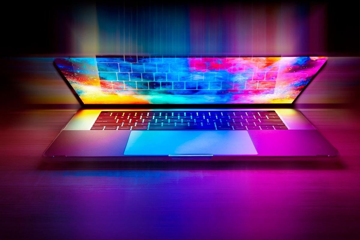Un ordinateur portable ouvert projette des couleurs néon sur le bureau