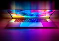 Un ordinateur portable ouvert projette des couleurs néon sur le bureau