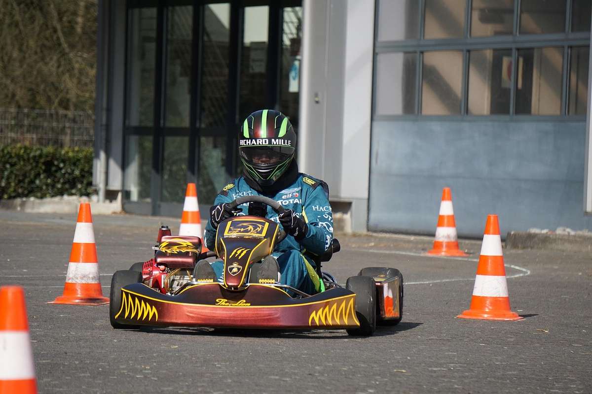 Un pilote en karting avec casque et kart navigue entre cônes orange